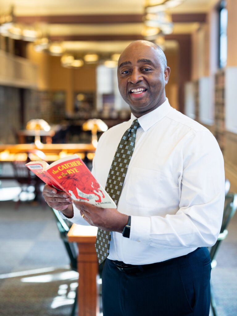 Photo of Felton Thomas Jr. standing in library reading a book