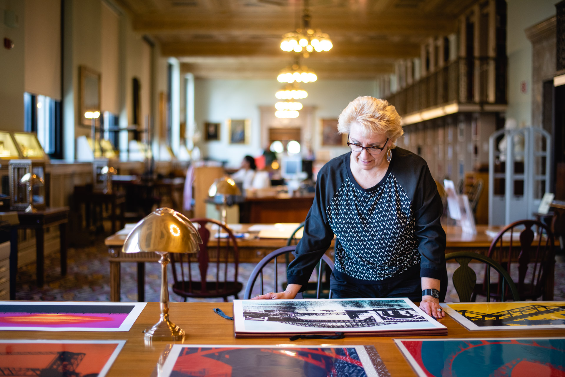 Pam Eyerdam (blond haired woman) standing at a table, looking at large art prints in the Special Collections Department.