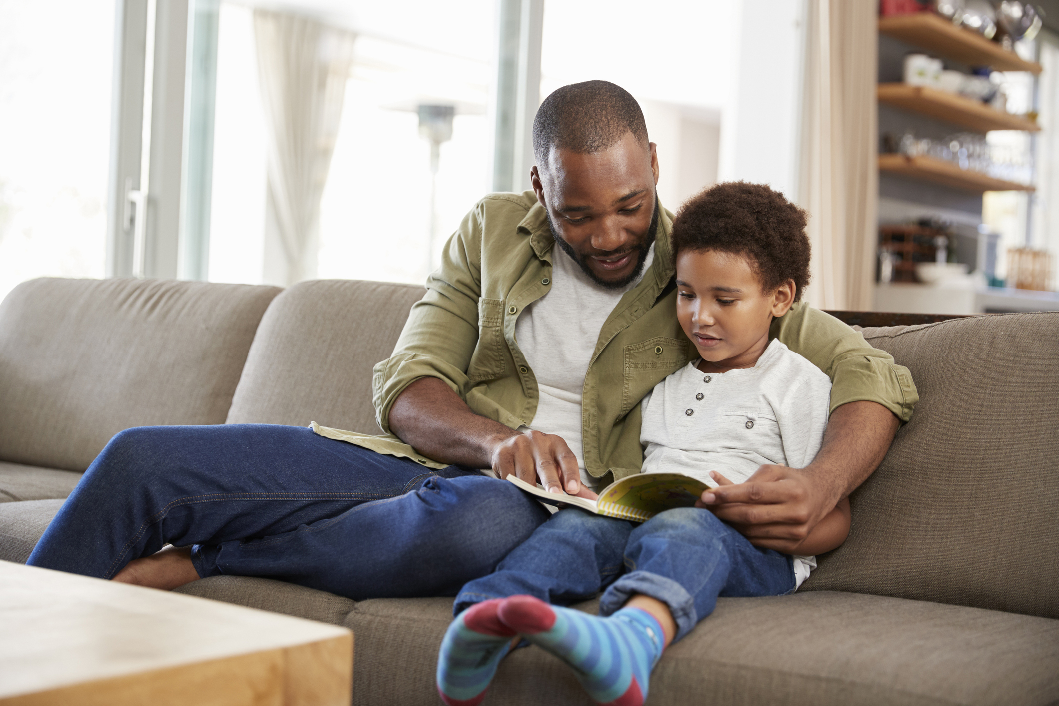 Father And Son Sitting On Sofa In Lounge Reading Book Together