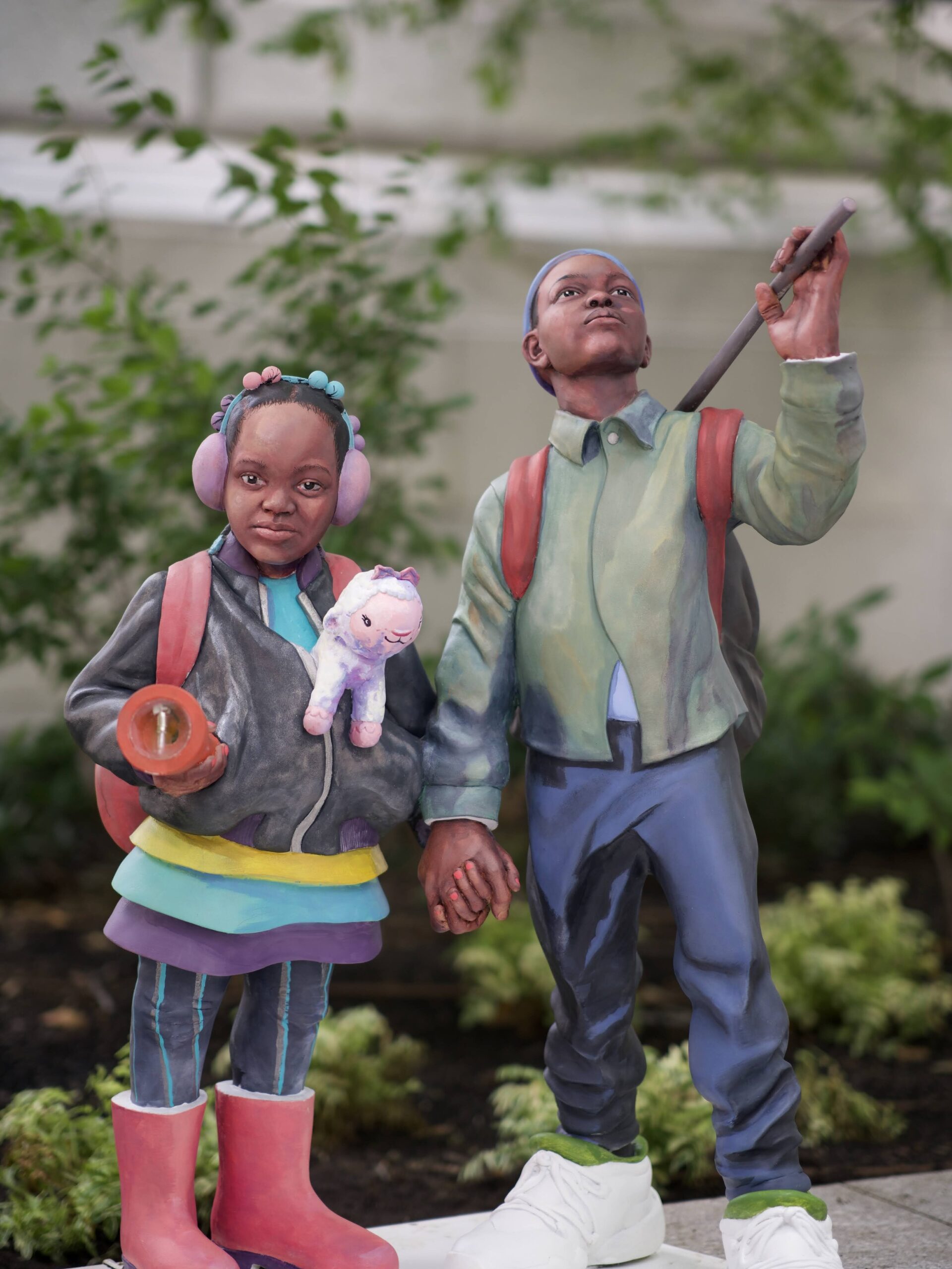 two sculptures, one of a young girl in a jacket and boots holding a flash light, the other of a young boy in a jacket and jeans holder her hand.